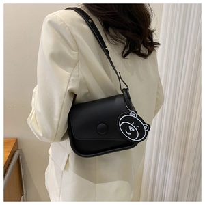 Detail of a black leather flap handbag with a round buckle and a minimalist bear charm