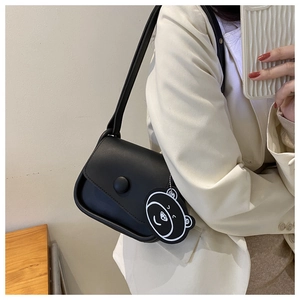 Shoulder view of a black leather flap bag with decorative buckle and cartoon bear charm