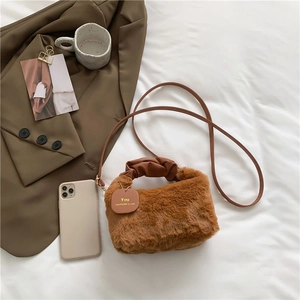Brown faux fur plush handbag with leather strap and decorative tag on white bedding