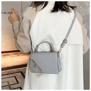 Detail of grey leather crossbody bag featuring gold metal bar and adjustable strap