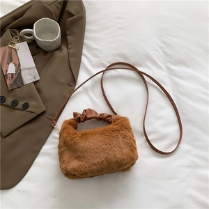 Brown plush crossbody bag with leather handle on a white bed alongside coffee blazer