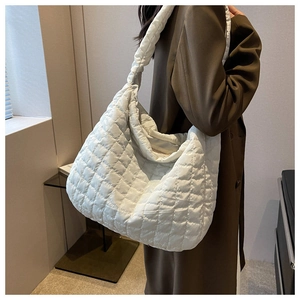 Detailed side view of a large white quilted shoulder bag on a model wearing a brown coat