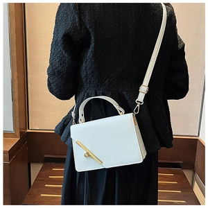 Detail of white leather crossbody bag with golden metal bar and twist-lock closure