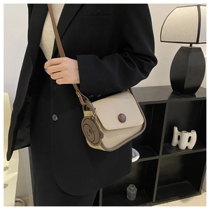 Chic beige crossbody bag with brown trim and cute bear charm shown on a black blazer