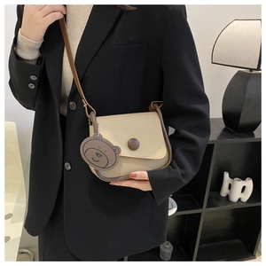 Detail of beige crossbody bag with brown trim and cute bear charm worn with black blazer