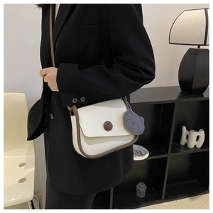 Detail of cream white leather crossbody bag with dark brown trim and a blue bear charm