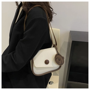 Detail of cream flap crossbody bag with brown trim and bear charm on a female model