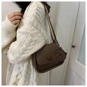 Detail of brown leather crossbody bag with round buckle and cute bear charm on a model