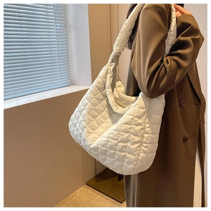 Detail of a large white quilted cloud bag shown on a model's shoulder in soft light