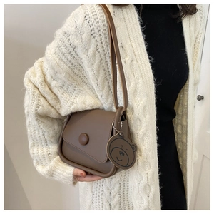 Detail view of deep brown matte leather crossbody bag with asymmetric flap and charm