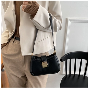 Detail view of the sleek black faux leather underarm bag with gold metal clasp on a model