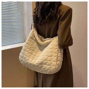 Detailed view of a white quilted puffer shoulder bag styled with a brown suit jacket