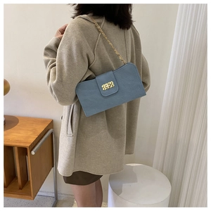 Sac bandoulière bleu à motif litchi avec chaîne dorée porté par un mannequin