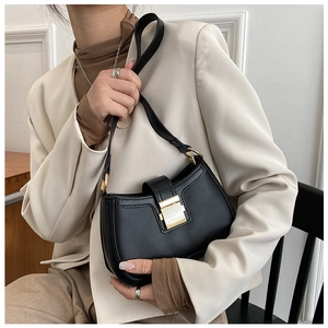 Detail of a black hobo bag featuring a gold square buckle on an elegant beige blazer