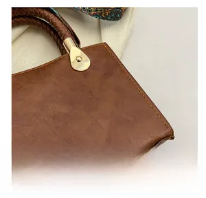 Dettaglio borsa a mano vintage marrone con cuciture a contrasto e manico intrecciato con foulard