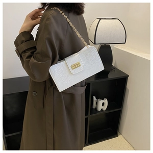 Détail du sac bandoulière en cuir gaufré blanc avec chaîne dorée sur un trench-coat
