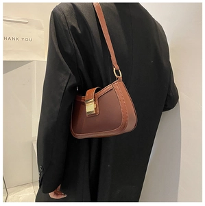 Detail of a brown leather underarm bag with a golden square buckle and matte finish