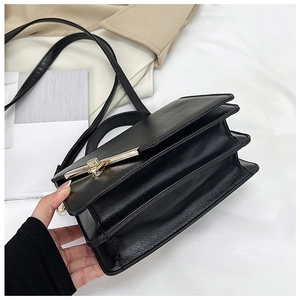 Detail of black leather crossbody bag featuring a triple-layer accordion design and gold T-bar buckle