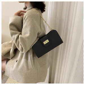 Détail d'un petit sac noir en cuir grainé avec chaîne dorée porté sur un manteau beige