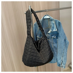 Detail of black quilted puffer tote bag hanging with denim jacket on wooden wall