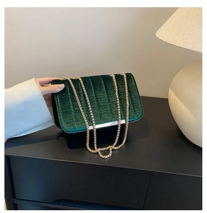 Close-up of dark green velvet handbag featuring vertical quilting and golden chain strap