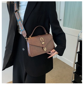 Dettaglio borsa a mano vintage in pelle marrone con chiusura a U dorata e tracolla stampata