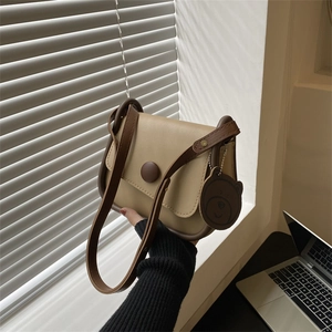 Chic beige crossbody square bag with brown trim and cute bear charm in natural light