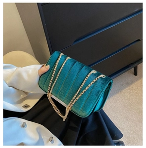 Detail of dark green velvet quilted bag with elegant gold chain strap and vertical seams