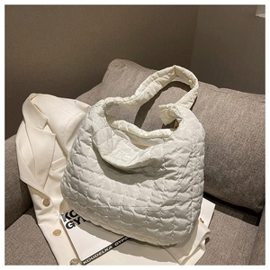 Close-up of a white quilted puffer shoulder bag on a grey sofa with minimalist decor