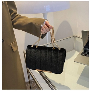 Detail of black velvet crossbody bag featuring vertical quilting and gold chain strap