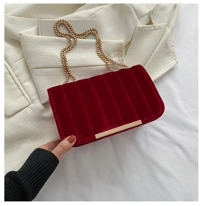 Close-up of red velvet quilted bag with gold bead chain and metallic trim detail