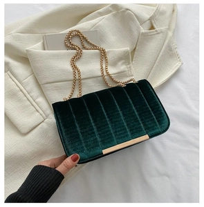 Detail of dark green velvet shoulder bag with gold chain on white blazer and books