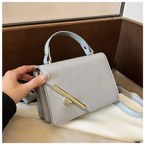 Close-up of litchi pattern leather handbag with diagonal gold metal clasp and top handle