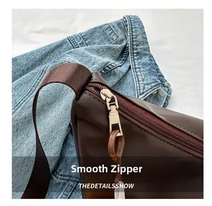 Detail of smooth silver metal zipper and brown woven strap on a soft leather bag