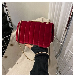 Detail of red velvet crossbody bag with vertical quilting and gold chain strap