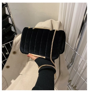 Detail of black velvet crossbody bag with vertical quilting and gold chain strap