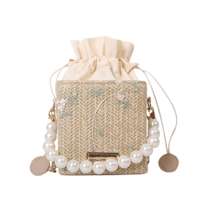 Straw bucket bag with floral embroidery and white pearl handle in minimalist white background