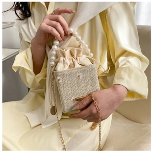 Detail of straw bucket bag featuring daisy embroidery, pearl handle and gold chain