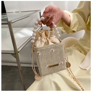 Detail of woven bucket bag featuring pearl handle and daisy embroidery with drawstring