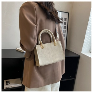 Dettaglio di borsa quadrata beige chiaro con manico intrecciato e tracolla fantasia