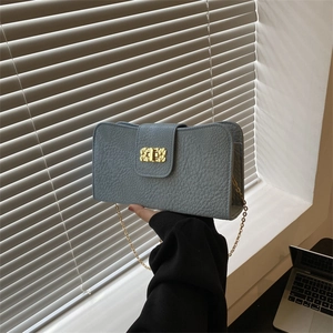 Sac bandoulière bleu clair en cuir grainé avec chaîne dorée, présenté à la main