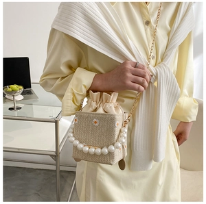 Detail of woven bucket bag featuring daisy embroidery, pearl handle, and gold chain strap