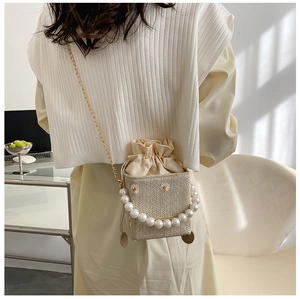Detail of woven straw crossbody bag with pearl handle and daisy embroidery on a model