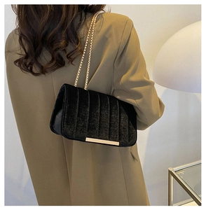 Detail of black velvet crossbody bag with golden chain and vertical quilted texture