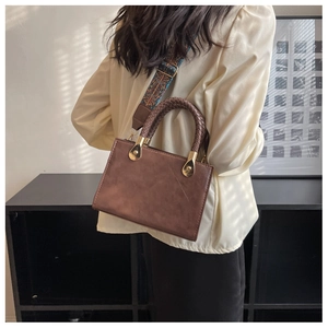 Dettaglio di una borsa marrone vintage con manici a cerchio intrecciati e tracolla etnica