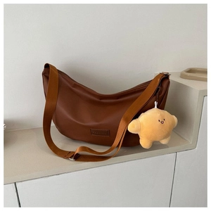 Close-up of brown crescent bag with wide nylon strap and star plush pendant