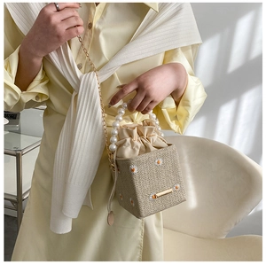 Detail of woven straw bucket bag featuring daisy embroidery and pearl handle strap