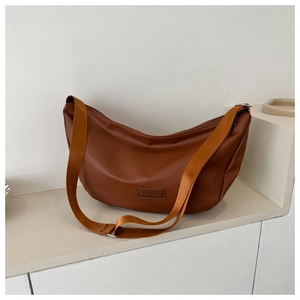 Detail of a brown crescent-shaped crossbody bag with soft faux leather and wide strap