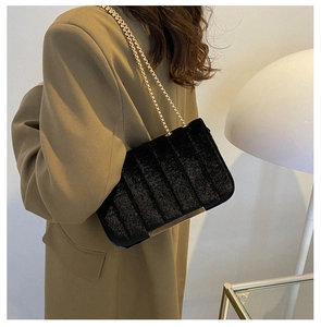 Detail of black velvet chain bag with pleated texture on olive blazer background