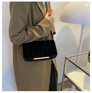 Detail of black velvet crossbody bag with gold chain strap on olive green blazer